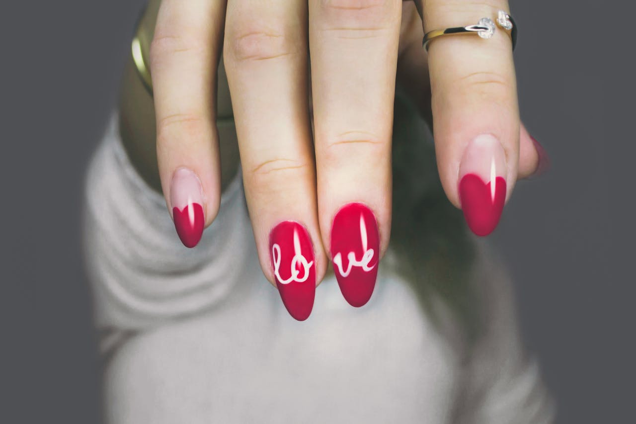 Vibrant red nails with love art on a womans hand, showcasing elegant style and design.