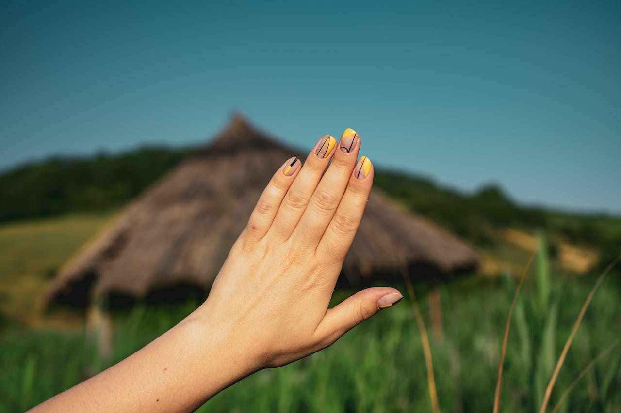 A close-up of a hand showcasing stylish nail art set against a rustic countryside background.